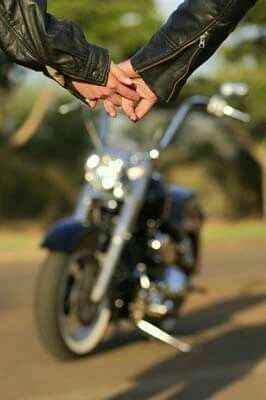 two people holding hands while standing next to a motorcycle