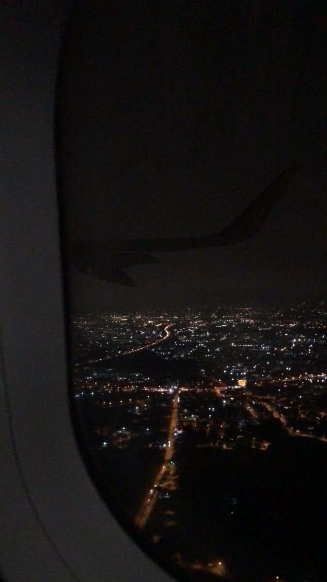 an airplane window with the view of city lights from it's wing at night