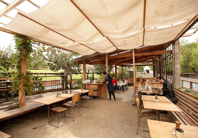 an outdoor dining area with wooden tables and benches under a large white awning over it