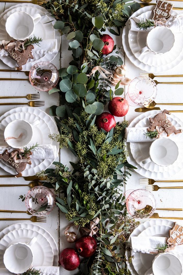 the table is set with plates, silverware and greenery as well as christmas decorations