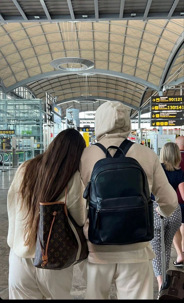 two people walking through an airport with backpacks on their backs and one person holding onto the back of another