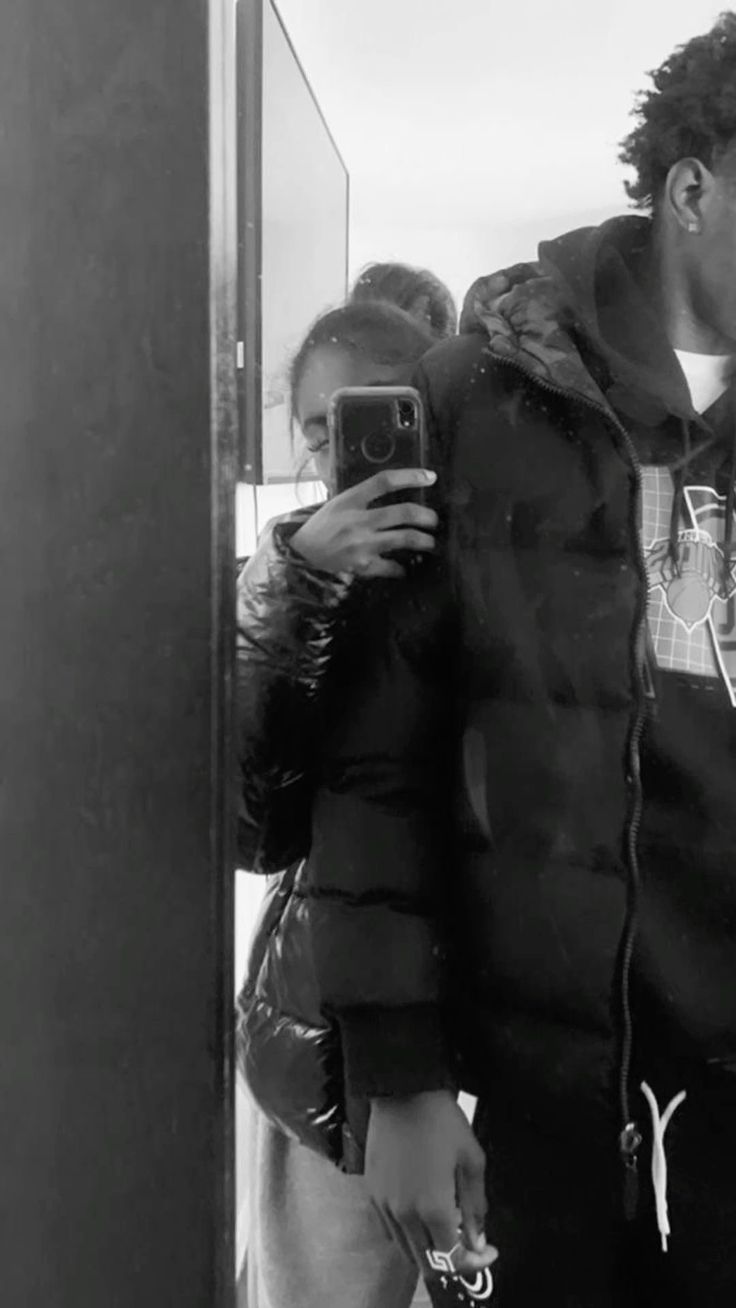 a man taking a selfie in front of a mirror with his cell phone while standing next to a woman