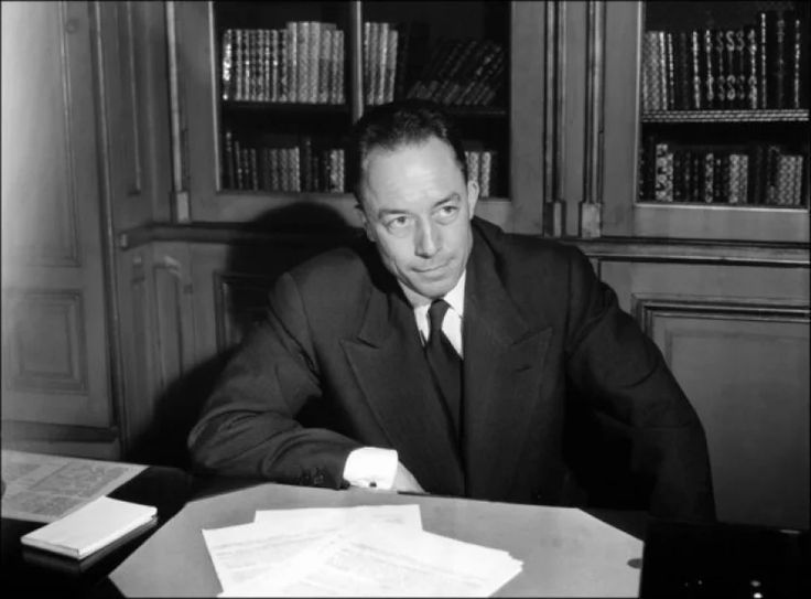 a man in a suit sitting at a desk with papers and pens on it, looking off to the side