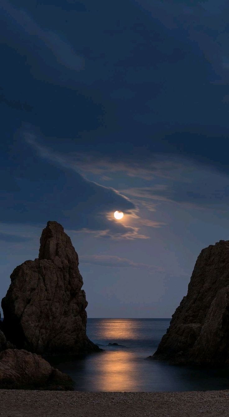 the moon is setting over the ocean and rocks