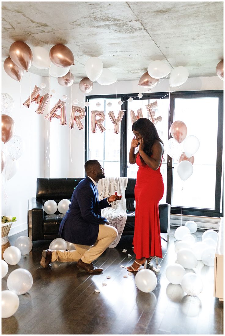 a man kneeling down next to a woman in a room filled with balloons and streamers