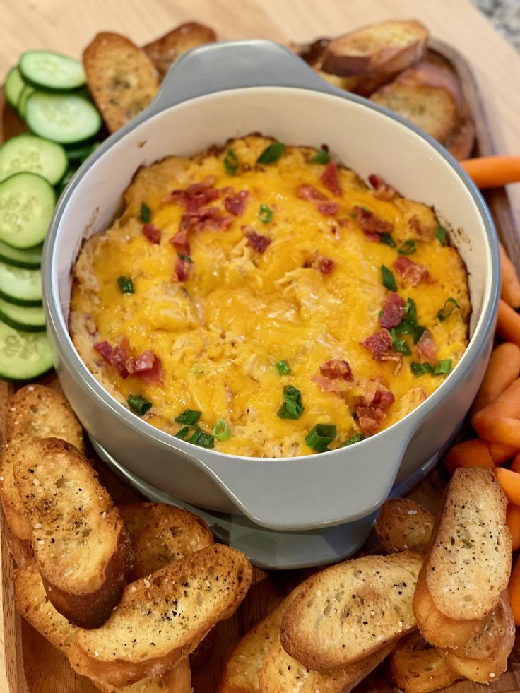 a bowl of dip surrounded by crackers, cucumbers and carrots