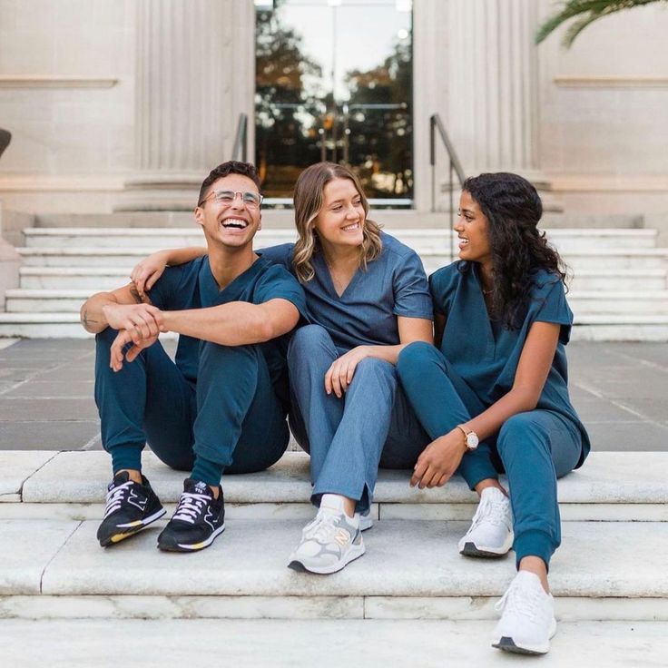 three people sitting on steps in front of a building smiling at each other with their arms around one another