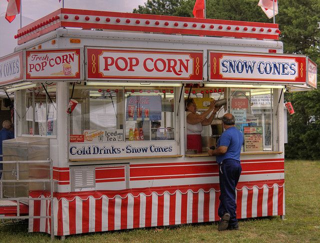 a man standing in front of a red and white popcorn cart