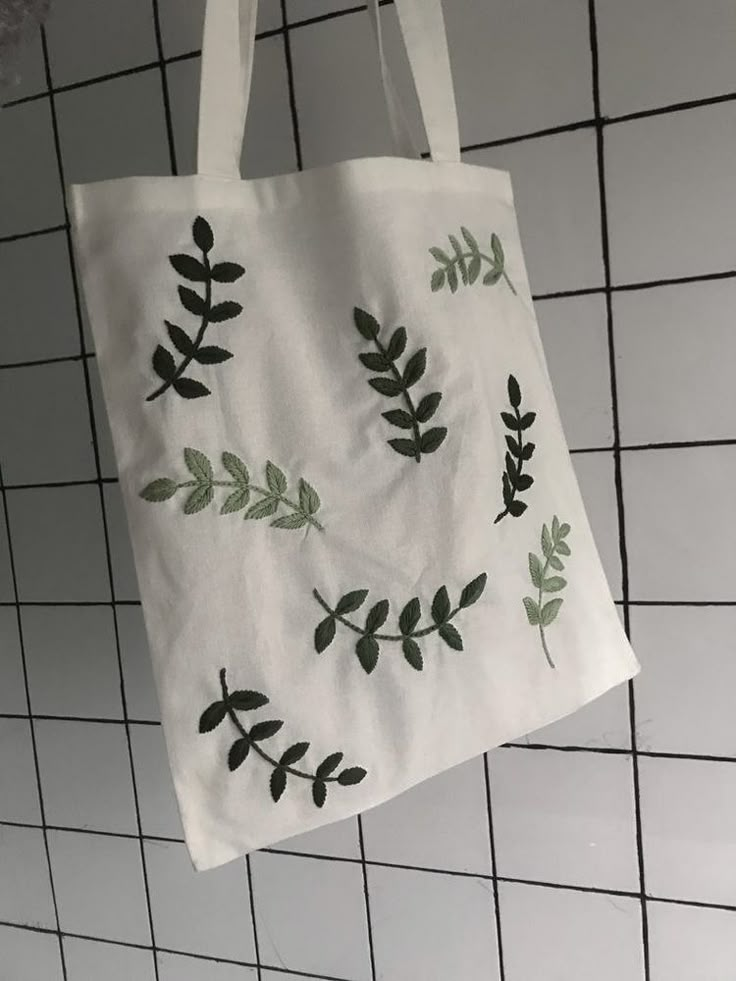 a white bag with green leaves hanging from it's side on a tiled wall