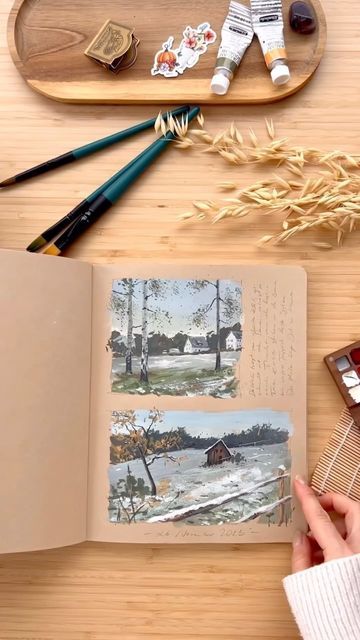 an open book sitting on top of a wooden table next to paint brushes and paints