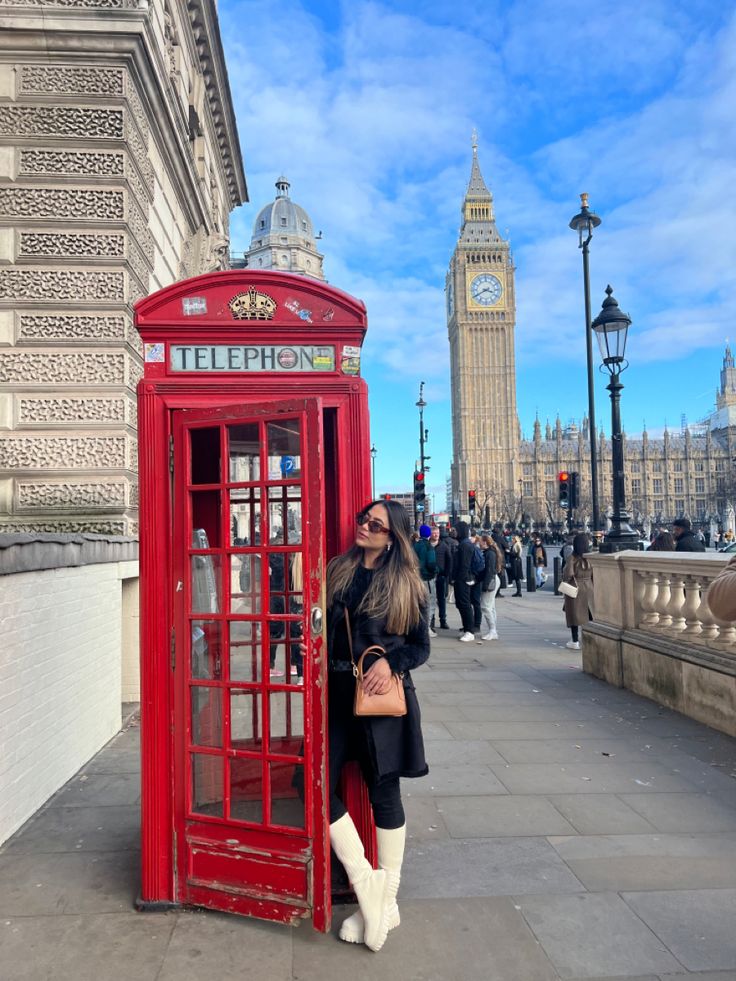 a woman standing next to a red phone booth