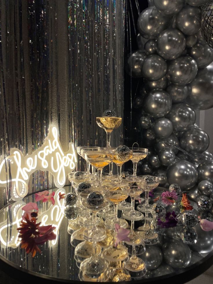 a table topped with lots of glasses filled with champagne next to balloons and confetti