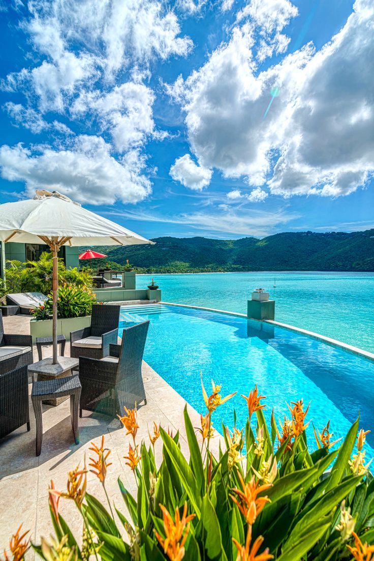 an outdoor pool with chairs and umbrellas next to the water, surrounded by greenery