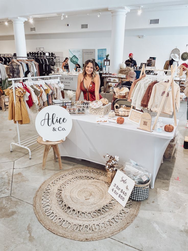 a woman standing next to a table with clothing on it in a room filled with people