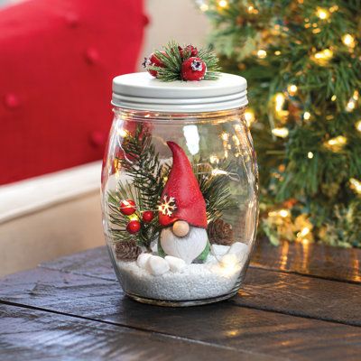 a glass jar filled with snow and christmas decorations sitting on top of a wooden table