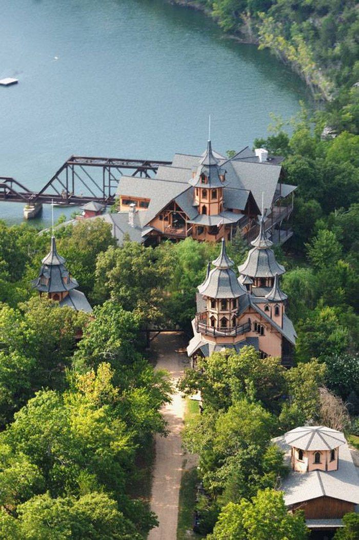 an aerial view of a house surrounded by trees and water with a bridge in the background