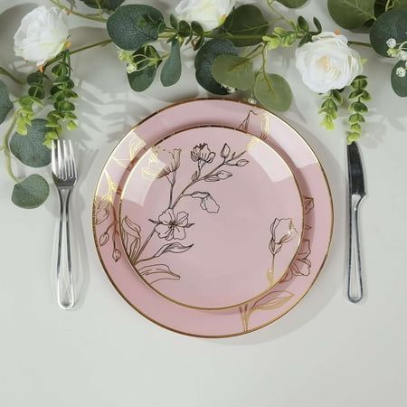 a pink plate with white flowers and greenery on it next to two silverware