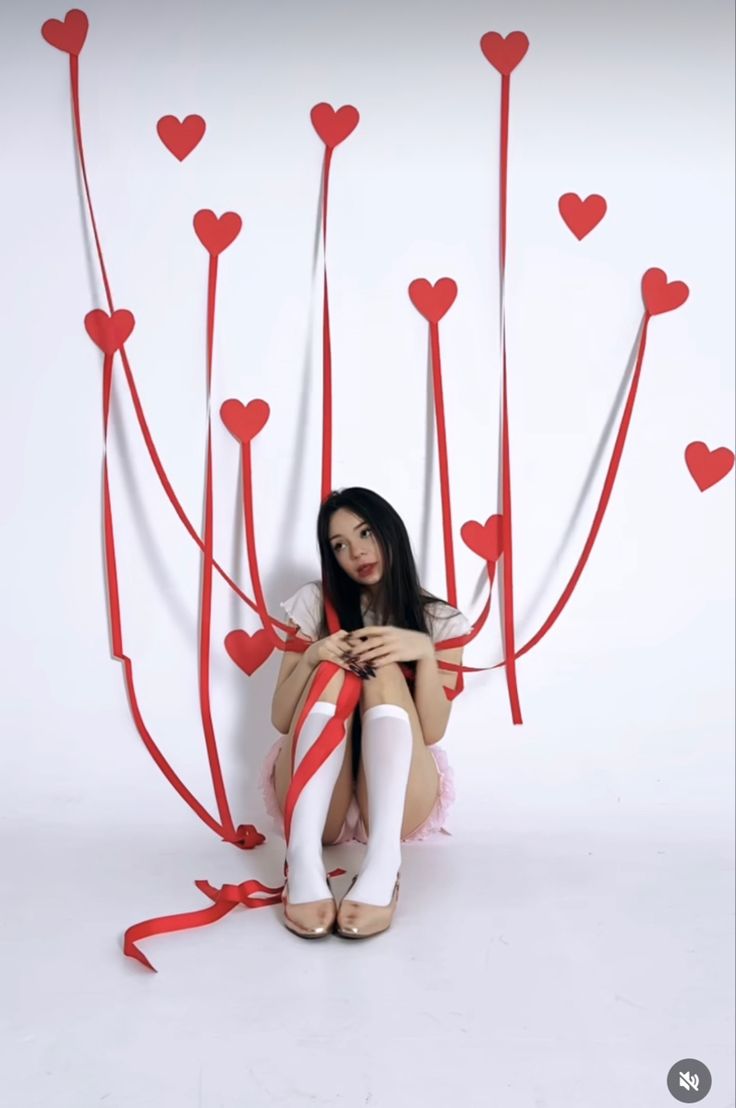 a woman sitting on the ground with red hearts attached to her legs and holding a cell phone