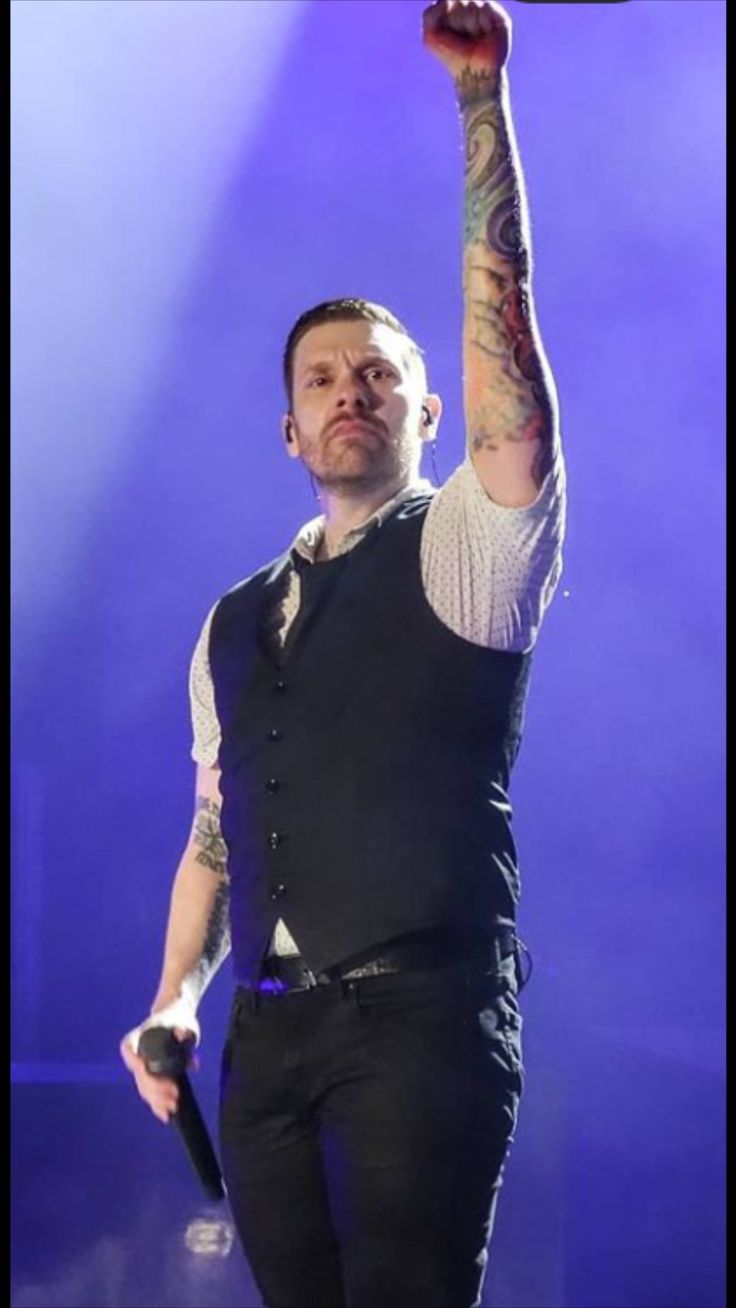 a man with tattoos on his arm holding up a microphone in front of purple light