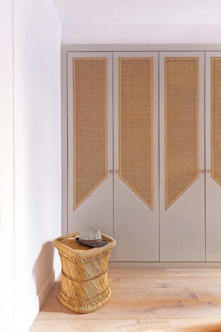 a basket sitting on the floor in front of some cupboards with woven doors behind it