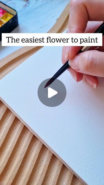 a person is drawing on paper with a pencil and watercolors in the background