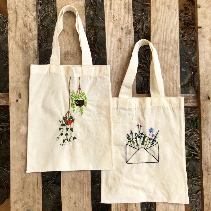 two embroidered bags sitting on top of a wooden table next to each other with flowers in an envelope