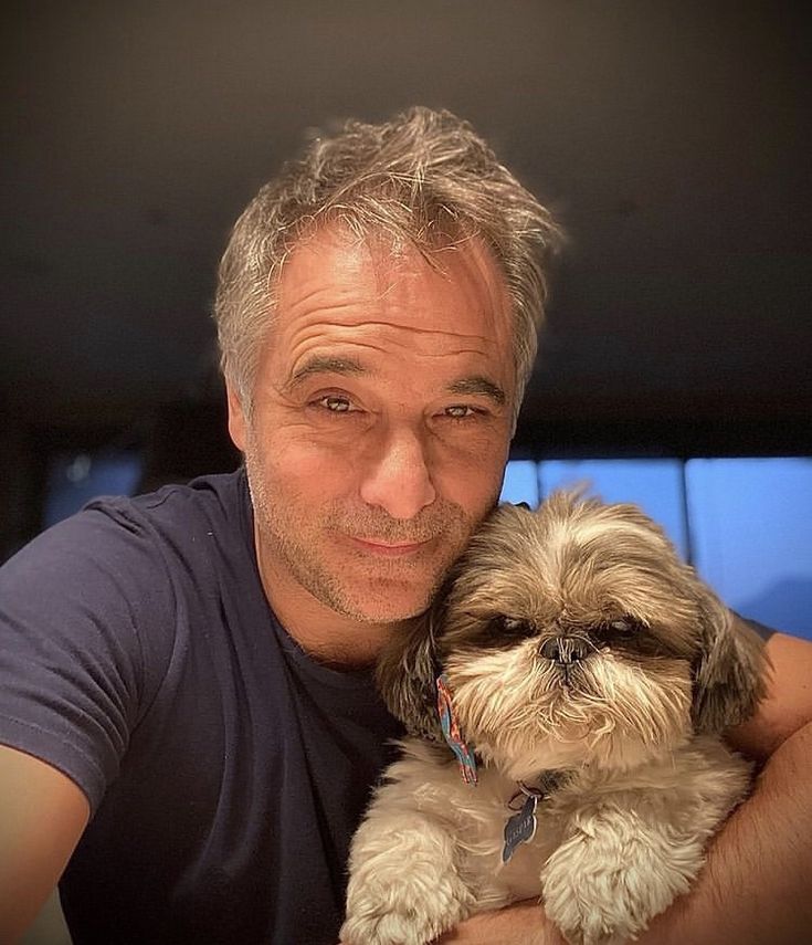 a man is holding a small dog in his arms and smiling at the camera while posing for a photo