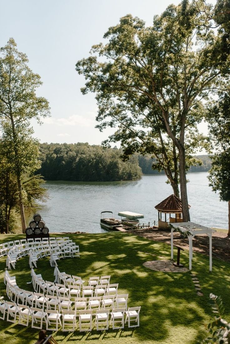 an outdoor ceremony set up on the lawn by the water with white chairs and umbrellas