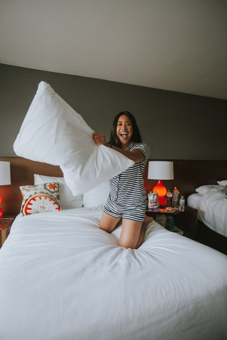 a woman sitting on top of a bed with pillows in her hand and smiling at the camera