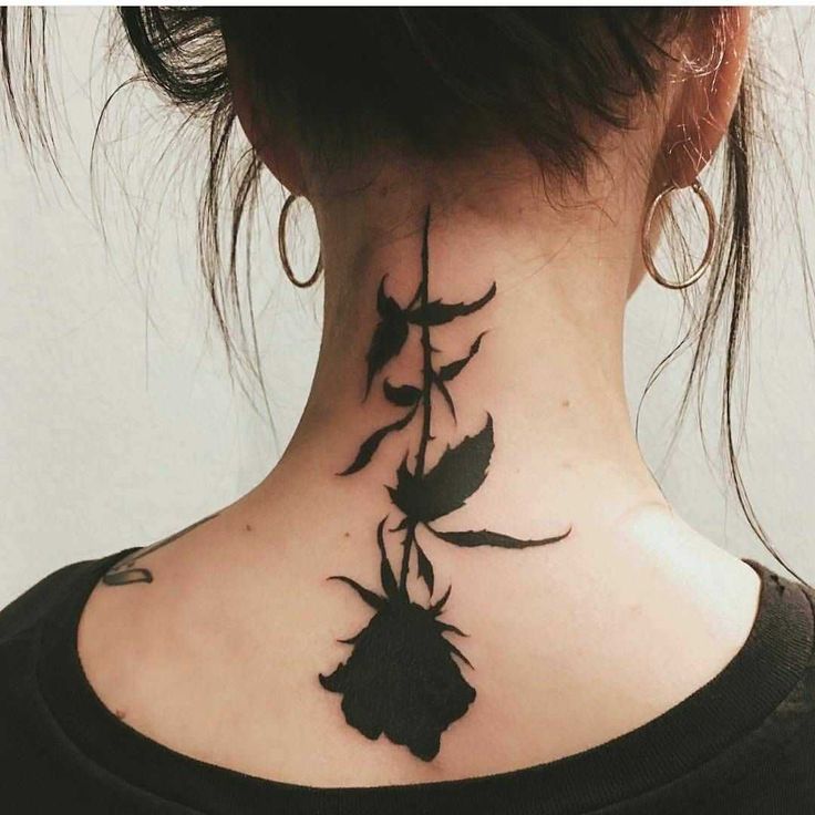 a woman's neck tattoo with black flowers on the back of her neck and behind her ear