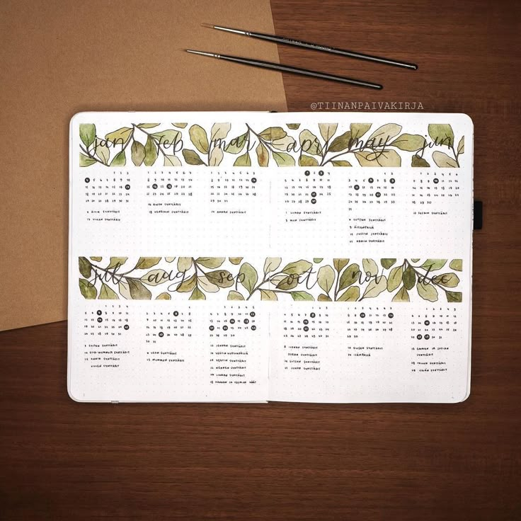 a calendar is sitting on top of a desk next to a pen and paper with leaves