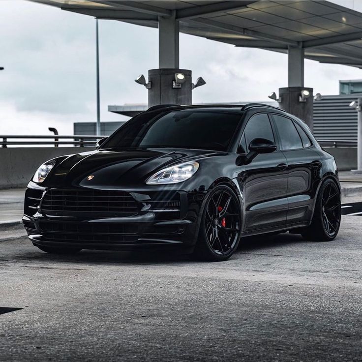 a black porsche cayen is parked in front of an overpass with lights on