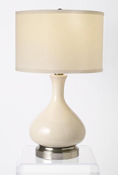 a white table lamp with a gold base on a clear shelf next to a white wall