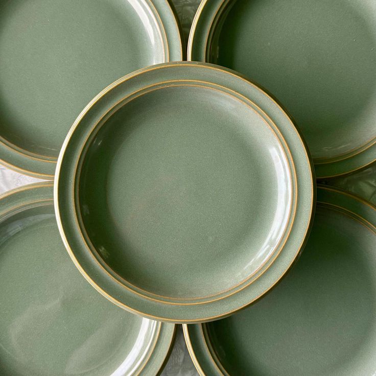 four green plates stacked on top of each other with gold trim around the rims