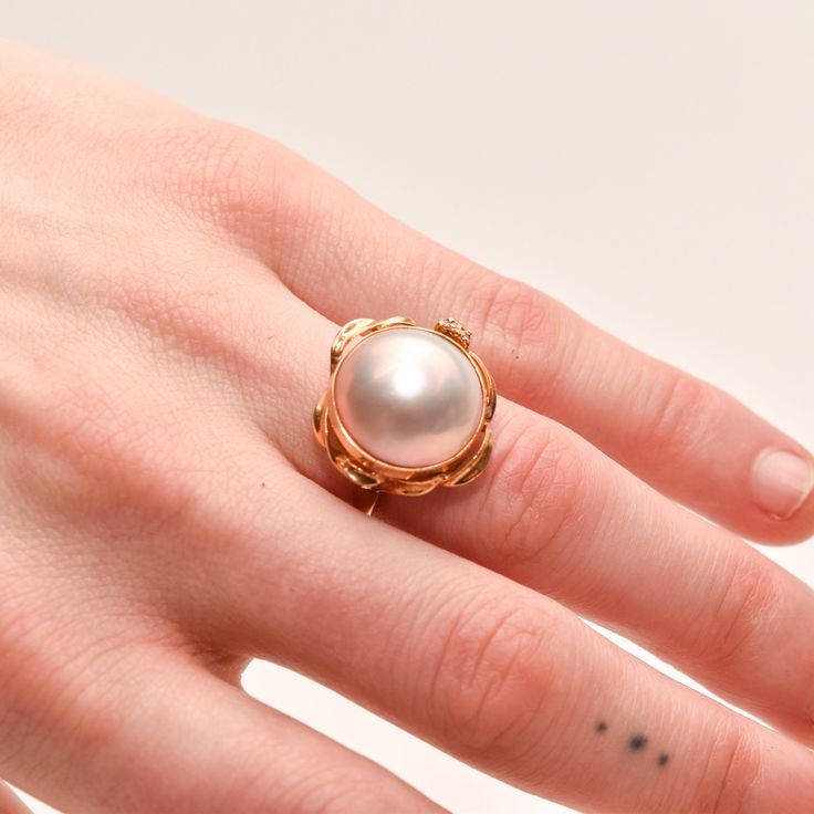 A gorgeous 18K mabe pearl cocktail ring with sparkling diamond accents. Features an iridescent mabe pearl over 15mm in diameter, mounted in a round bezel setting with gold ribbon trim and two flanking diamond accents. The setting has an openwork underside and sits atop a straight yellow gold band with a polished finish.  The inner band is hallmarked '18K' and the gold has been tested for authenticity. In great vintage condition with minimal wear and discoloration.  **This listing contains photographs of the actual item you will receive. Please look closely at the pictures as they are part of the product description. Every piece is cleaned, polished, examined, and described to the best of our ability and we encourage you to reach out with any questions.** Condition: Good Ring size: 6 US Pea Pearl Cocktail Ring, Yellow Gold Cocktail Ring, Mabe Pearl, Gold Cocktail Ring, Gold Cocktail, Luxury Rings, Sparkling Diamond, Gold Ribbon, Rings Cool