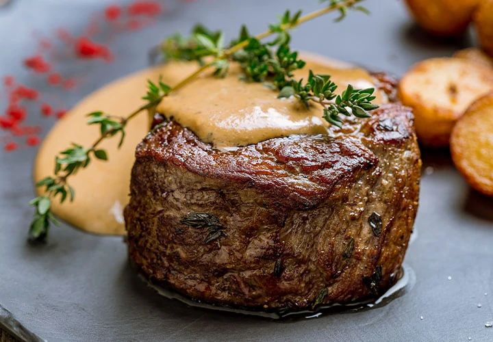 a steak with gravy and potatoes on the side, ready to be eaten