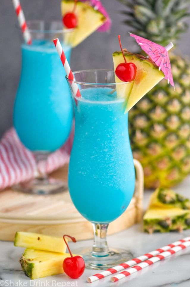 two glasses filled with blue liquid and topped with pineapples, cherries and umbrellas