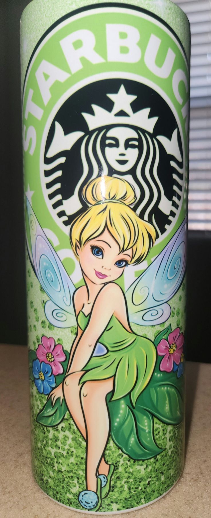 a starbucks cup with a fairy tinker sitting on top of it's side