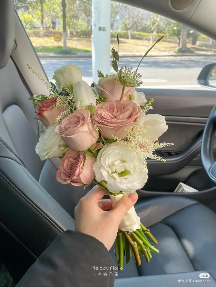 a person holding a bouquet of flowers in the back seat of a car with their hand on the steering wheel