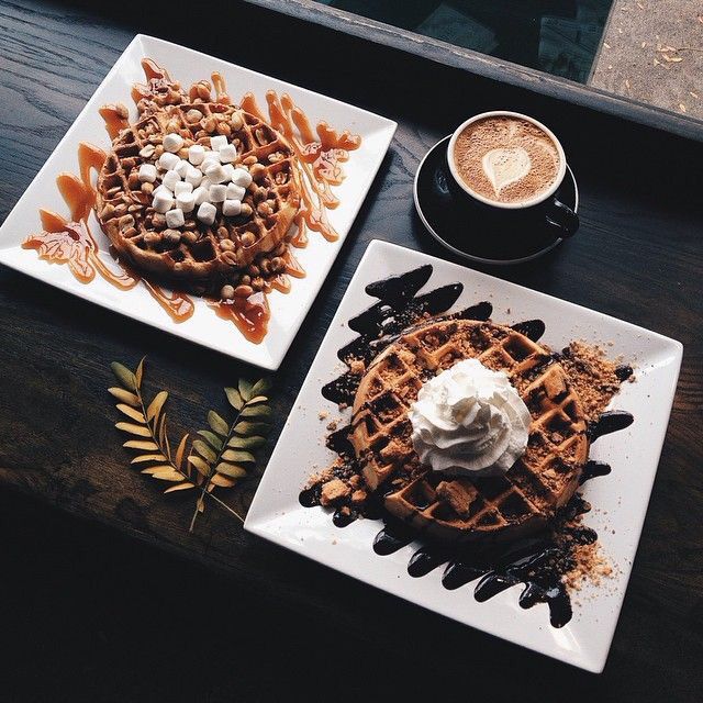 two plates topped with waffles next to a cup of cappuccino