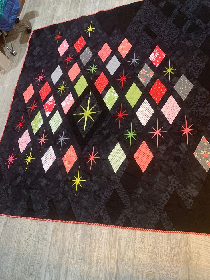 a black quilt with red, green and yellow stars on it sitting on the floor