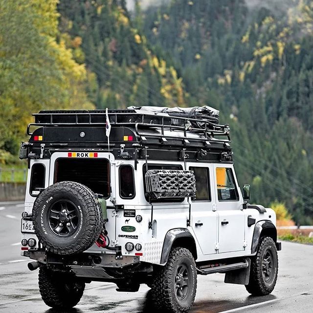 a white four door jeep driving down a wet road with trees in the back ground