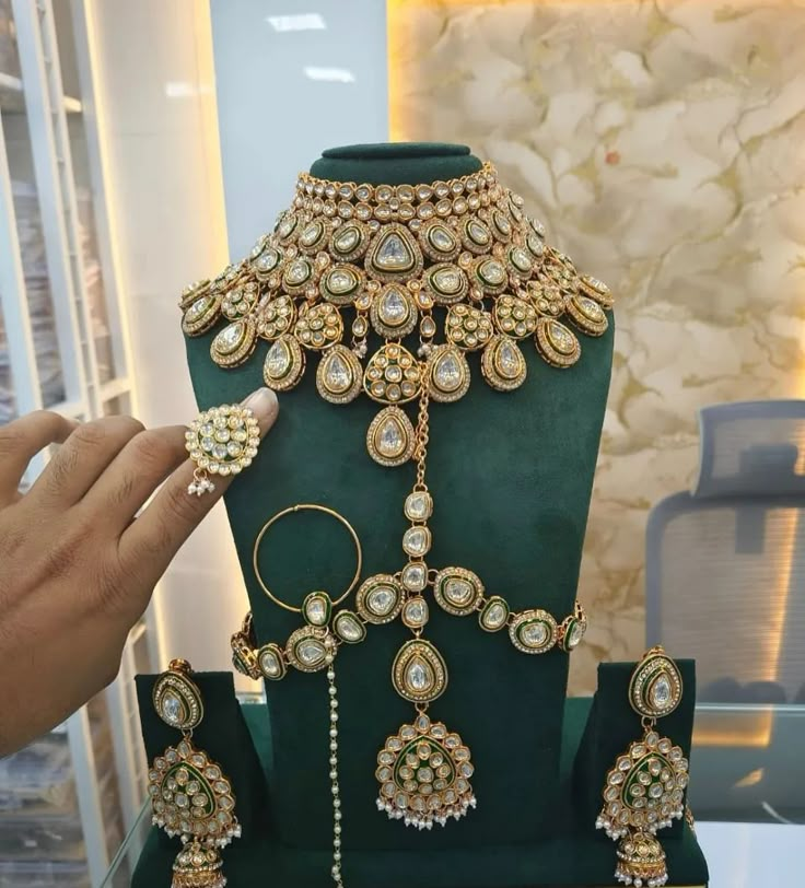 a green display case with gold jewelry on it's sides and a hand reaching for the necklace