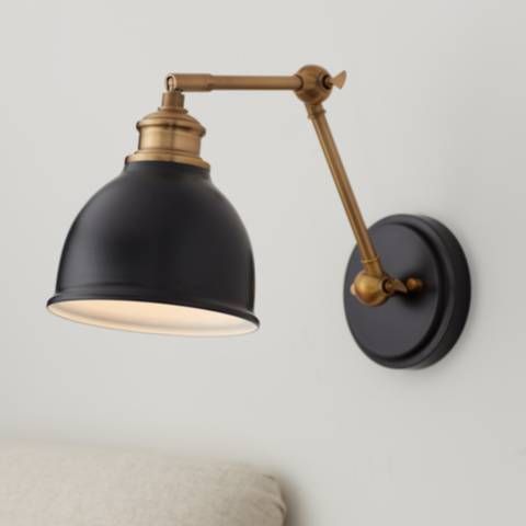 a black and gold wall light mounted on the side of a white wall next to a bed