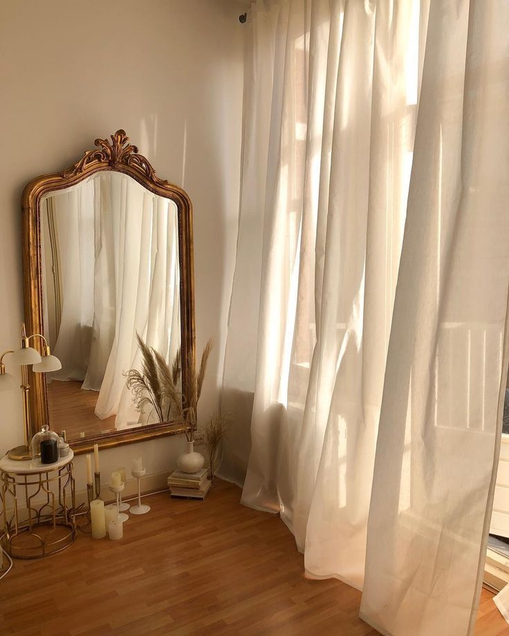 an image of a room with white curtains and a mirror on the floor in front of it