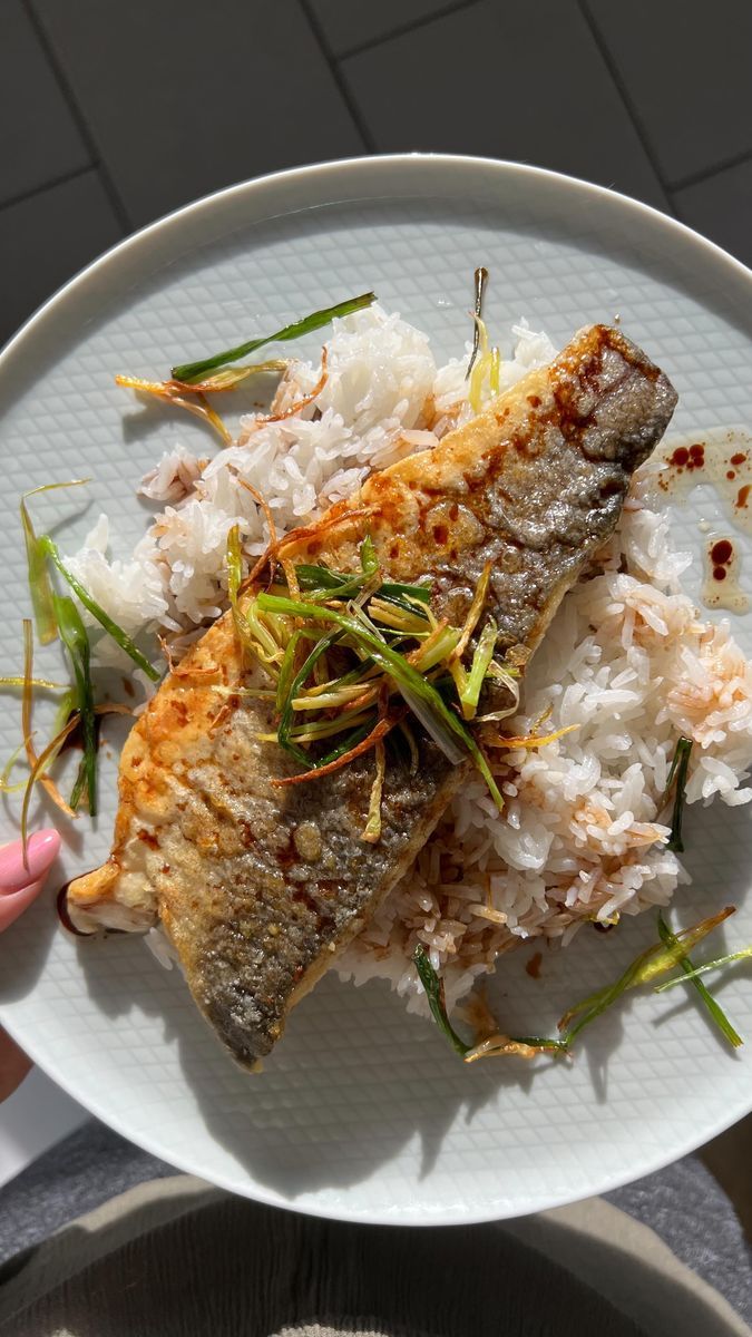 someone holding a white plate with some fish and rice on it in front of the camera