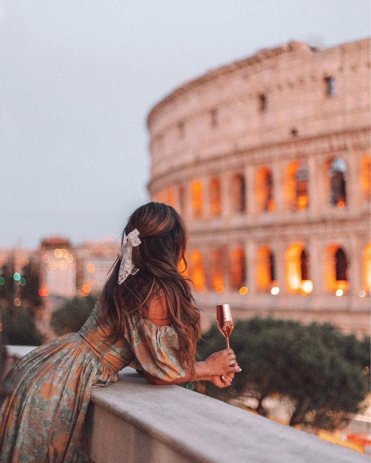 a woman sitting on a ledge looking at the roman colossion in rome, italy