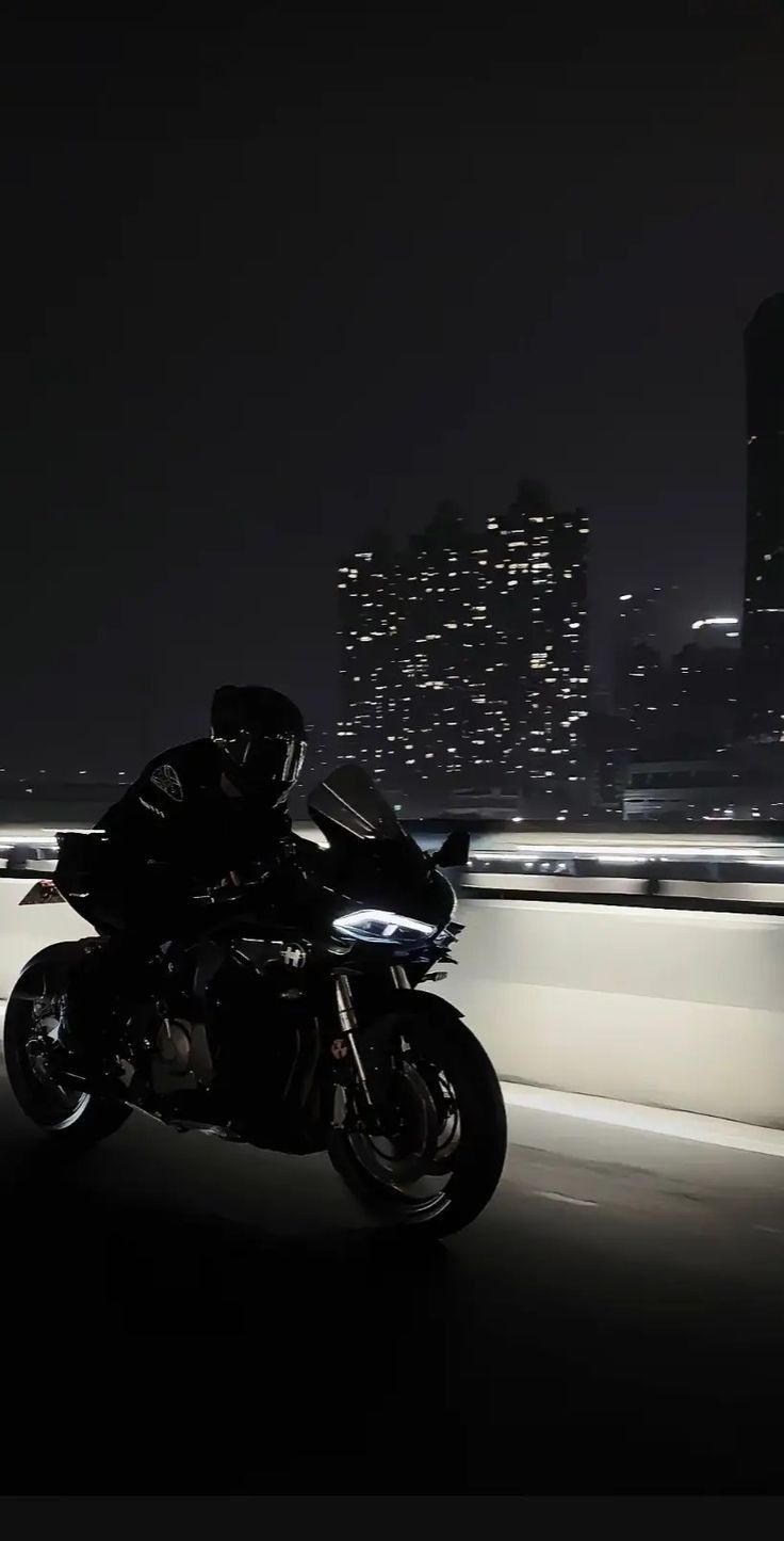 a man riding a motorcycle down a highway at night with city lights in the background