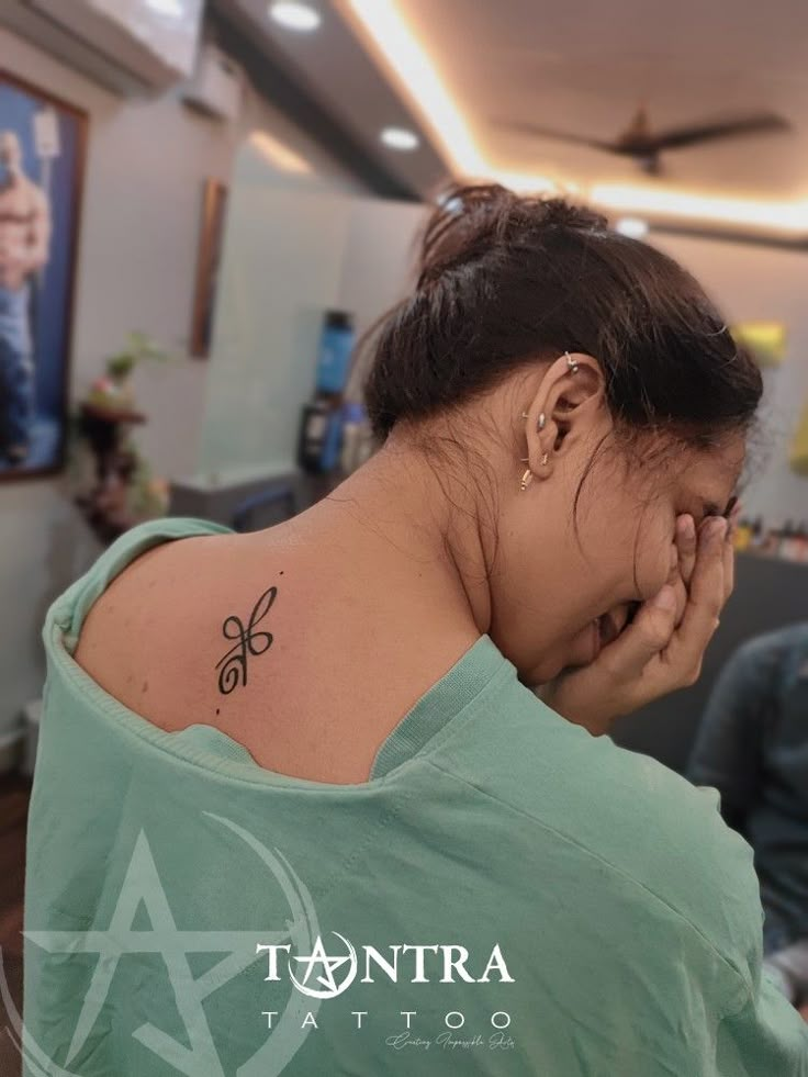 a woman with a small tattoo on her upper arm and behind her head is looking at the camera