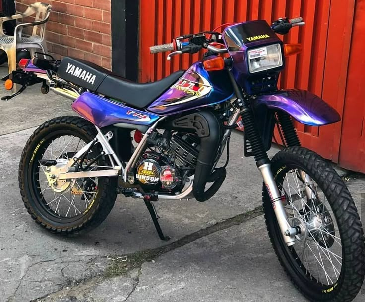 a purple and black motorcycle parked next to a red building on the side of the road